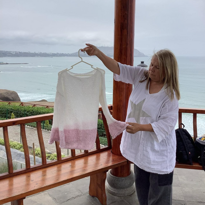 Person holding a hanger with a white garment on a balcony overlooking a beach.
