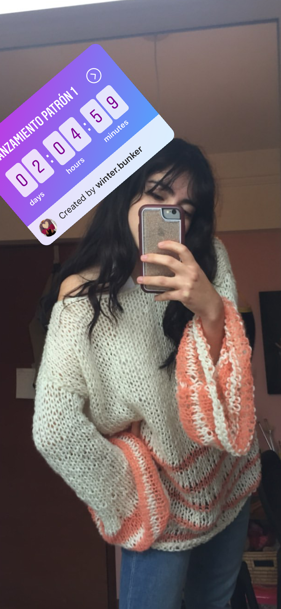 Person wearing a patterned sweater taking a mirror selfie with a phone.